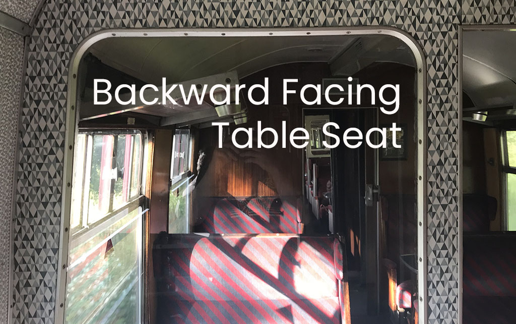 An interior train window looking down a carriage of red seats with white text that reads 'Backward Facing Table Seat'