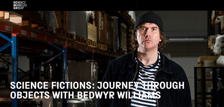 Artist Bedwyr Williams photographed in a Science Museum storage room. He wears a beanie hat and a stripy T-shirt.